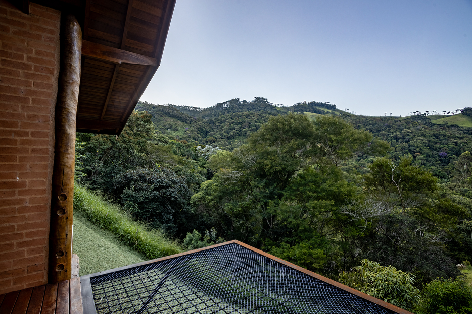 Wooden deck with black chair and table next to a cabin, overlooking a lush green mountainous landscape with clear sky and a large yellow plant in the foreground.